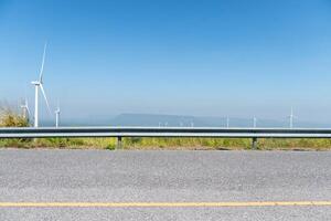 Horizontal view asphalt road with guard lens. Wind turbines tower over a lush forest. photo
