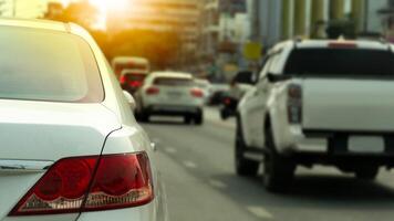 Rear side of white car driving on the asphalt road. Forward vehicular traffic. Blurred of tall buildings in the background. Light shines from behind. photo