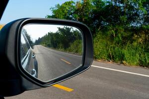 Inside view of mirrors wing. Rear view of a gray car with asphalt road. photo
