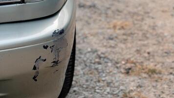 Car bumper with visible scratches and paint damage. Gold colored bumper has dark scuff marks. suggesting a collision or scrape. Background is a blurred textured surface possibly a road or pavement. photo