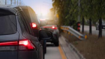 Rear side of cars on the road with turn on brake light. Background is blurred suggesting movement and depth with glimpses of red tail lights and sunlight filtering through trees. photo