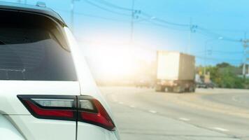 Car rear close up tail light. Blurred background showing a large truck on a sunny road. Bright sunlight creates a hazy effect suggesting a warm day and highway travel. photo
