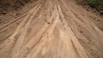 Dirt road or path with visible tire tracks indicating vehicle passage. The ground is rough and textured with a mix of light and dark soil suggesting a rural or unpaved setting. photo