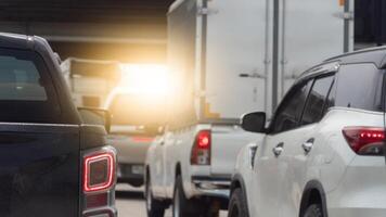 Congested traffic scene with multiple vehicles. including cars and a large truck. tightly packed on a road. A bright light source in the background creates a strong glare. with cement bridge on top. photo
