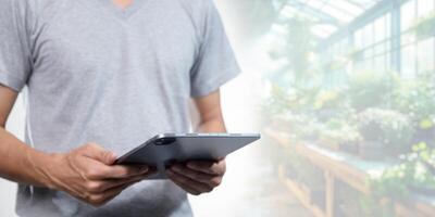 Man Using Tablet in Greenhouse with Lush Plants in Background photo