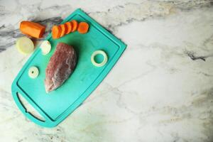 A raw piece of pork with vegetables, onions and carrots lies on a cutting board with space for copyspace text photo