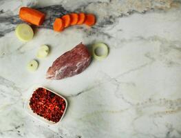 raw meat, vegetables, onions, carrots, seasoning on the table with space for text, copyspace, top view photo