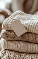 Stack of cashmere sweaters in beige and white with an empty tag resting on top in natural light photo