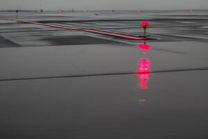 Rain-soaked runway reflecting jet nose with a striking red navigation light at dusk photo