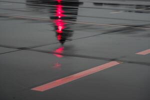 Jet nose reflection on a rain-soaked runway with red navigation light accent photo