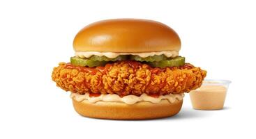 A fried chicken sandwich with pickles and a cup of ketchup photo