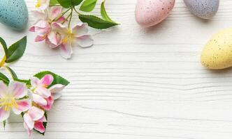 Easter eggs and flowers creating a frame on wooden background photo