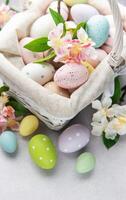 Pastel colored easter eggs overflowing from a wicker basket decorated with spring flowers on concrete photo