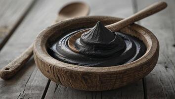 Natural activated charcoal paste in rustic bowl with wooden spoon on wooden table photo