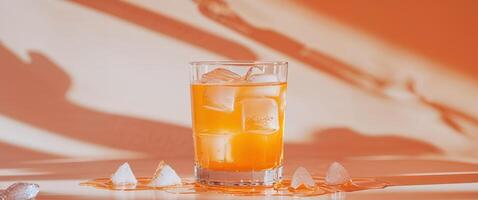 Refreshing Orange Drink with Ice in a Clear Glass on Orange Background. photo