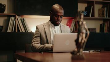 Justice and law concept. African American Male judge in office working with, computer laptop and docking keyboard, at table in the evening, late night. video
