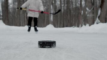 A teenager rides up to the ice rink and practices his stick-handle skills on outdoor winter rink. The puck is on the ice. Slow motion video