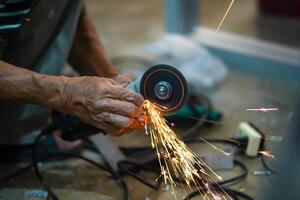 Closeup hands of the master saw the metal holding electric angle grinder working with sparks in metalworking photo