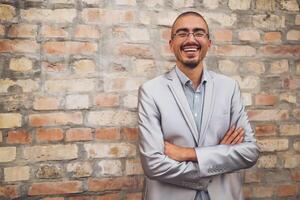 Adilt man in suit is standing in the front of brick wall, looking at camera and smiling. photo