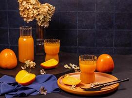Fresh persimmon juice with ripe persimmons and dried flowers on dark background photo