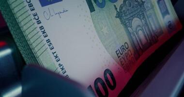 A close up of a bank note on a money counting machine with a red light video