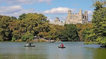 New York. US. 03.02.2025 The Lake in Central Park with rowboats gliding across the water, lush autumn foliage surrounding the tranquil scene, historic Upper West Side buildings in the background video