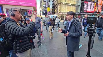 New York. US. 03.02.2025 Live recording at Times Square, New York City, with a content creator interviewing a speaker, bustling urban backdrop featuring LED billboards, pedestrians, and cyclists in video