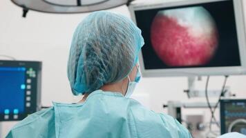 Back view of surgeon looks at monitors while preforming operation in hospital operating theater, female surgeon operating patient working with surgical laparoscopy instruments. Gynecology video