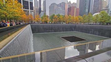 New York. US. 03.02.2025 9-11 Memorial South Pool with cascading waterfalls, reflecting the absence and remembrance of lives lost, surrounded by autumn trees and towering skyscrapers in Lower video