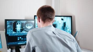 Man, doctor radiologist sits in control room and watches at monitors with displayed scans results. Professional doctor controls MRI or CT or PET scan video