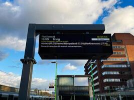Modern train station platform sign displaying schedule under a cloudy sky photo