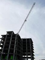 Tall construction crane beside an unfinished building under a bright cloudy sky photo
