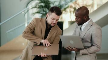 Two business men, an African American and a European, discuss a project before a conference in the hallway of a modern office building. Concept professional atmosphere, collaboration, and technology video