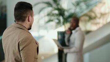 Two multiracial business men work and converse in the lobby of a modern business center, preparing for a business meeting or conference. Concept business solutions video