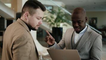 Two business men, an African American and a European, discuss a project before a conference in the hallway of a modern office building video