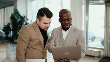 Two business men, an African American and a European, discuss a project before a conference in the hallway of a modern office building. Concept professional atmosphere video