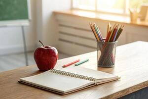 Back to school essentials with an apple, notebook, and colored pencils on a desk near a window photo
