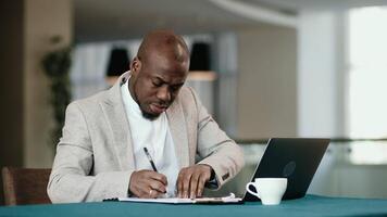 Smiling African professional businessman making call on cellphone using laptop computer communicating with client. Happy young business man sales manager talking on mobile phone working in office video