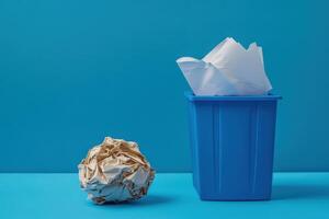 A blue trash can sits next to a pile of paper photo