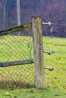 Broken wire mesh fence leaning on weathered wooden post in rural landscape photo