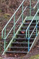 Green metal staircase with handrail showing signs of decay and litter photo