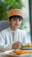 A young boy sitting at a table with a plate of food photo