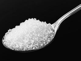 Close-up view of granulated sugar on a spoon against black background photo