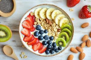 Colorful fruit and yogurt bowl with granola and nuts on wooden table photo