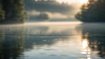 Dew drops glisten on a spider web above a tranquil lake at dawn surrounded by misty trees photo