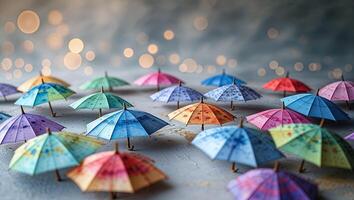 Colorful miniature umbrellas arranged on a textured surface with soft bokeh lights in the background during evening hours photo