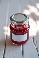 Homemade raspberry jam in a glass jar placed on a rustic wooden table in bright natural light photo