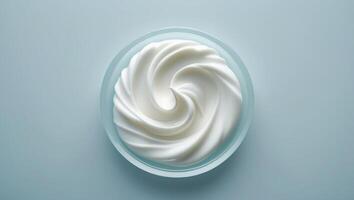 Whipped cream swirls in a clear bowl on a light blue background, showcasing a delicious dessert topping photo