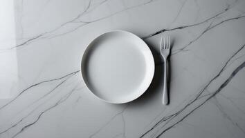 Simple white plate and fork arranged on a marble table surface in a modern dining setting photo
