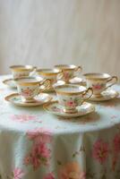 Elegant tea cups with rose pattern arranged on a table covered with a floral tablecloth photo